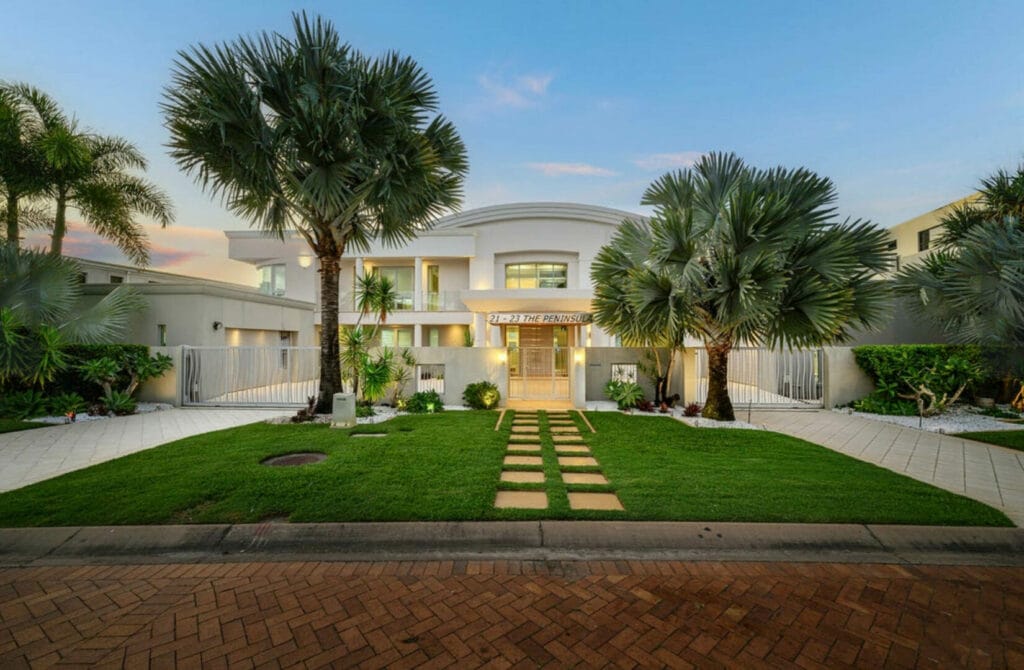 Luxury home with manicured lawn, palm trees, and paved walkway to entrance